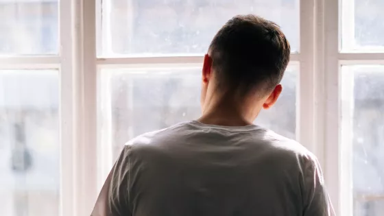 A young man, pictured from behind, looks through a bright window.