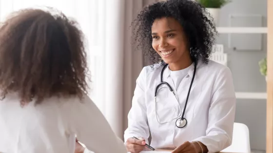 A medical professional smiles at a younger patient during a consultation.