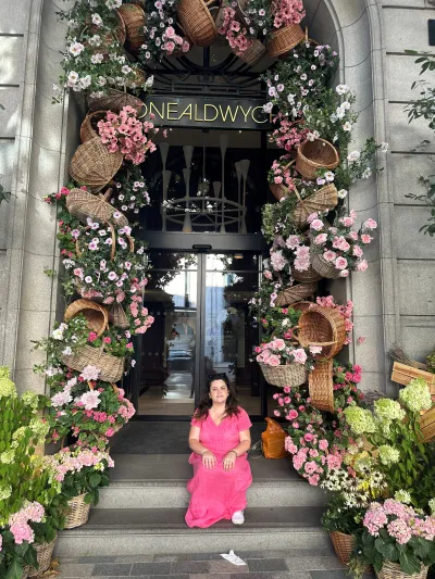 A young woman, Emma, sits in a doorway decorated with pink flowers.