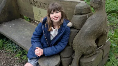 A girl sits on a bench in a forest.