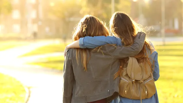 Two female friends stand arm in arm.